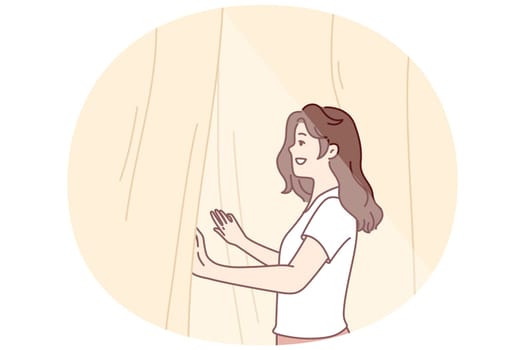 Smiling woman looks out window opening curtains and enjoying rays of summer morning sun. Girl opens curtains rejoicing at new sunny day after waking up in morning or dreams of going for walk