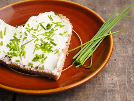 Delicious organic bread with cream cheese and chives on a rustic plate, healthy food concept