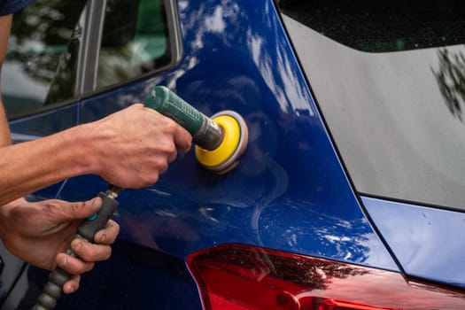 A man is polishing a car with a yellow brush. The car is blue and shiny.
