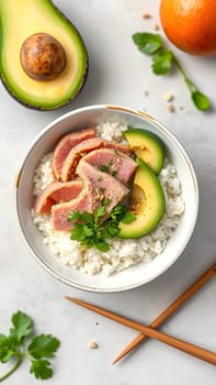 A vibrant bowl features sliced fresh tuna, creamy avocado, and fragrant rice, garnished with cilantro. The setting includes scattered cilantro and an orange, creating a colorful, appetizing layout.