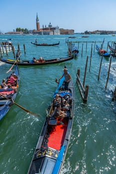 Venice, Italy - July 26, 2024: Gondolas against the San Giorgio island in Venice, Italy. Gondola is the most attractive tourist transport in Venice. Traveling and vacation in sunny Venice.