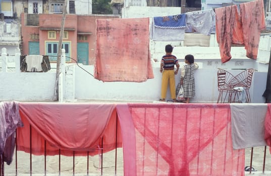 Children are playing on a balcony in the old Town in the Jaisalmer Fort with the city of Jaisalmer in the Province of Rajasthan in India.  India, Jaisalmer, January, 1998