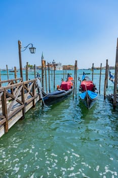 Venice, Italy - July 26, 2024: Gondolas against the San Giorgio island in Venice, Italy. Gondola is the most attractive tourist transport in Venice. Traveling and vacation in sunny Venice.