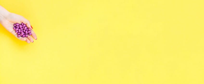 Woman hand holding purple pills handful isolated on bold yellow background with copy space. Template for feminine beauty blog social media. Female healthcare or suicide prevention concept