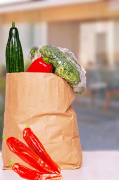 Closeup of a brown paper shopping bag with fresh vegetables and paprika on table over abstract blurred house background. Space. Concept of strengthening the immune system.