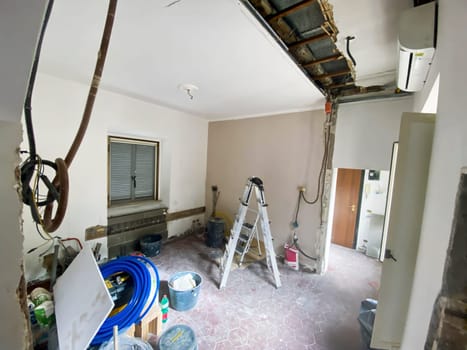 Interior view of a room under renovation with exposed wires, tools, and construction materials scattered around, showing ongoing work