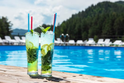 Two Mojito cocktail with lime and mint in highball glass on the swiming pool background. Concept of summer relaxing