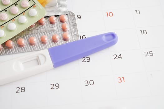 Pregnancy test with birth control pills and condom for female on calendar, ovulation day.
