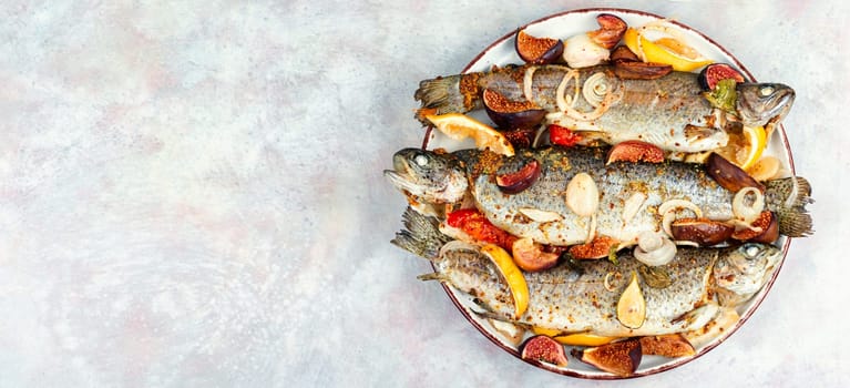 Baked whole river trout with ripe figs on a concrete kitchen table. Flat lay