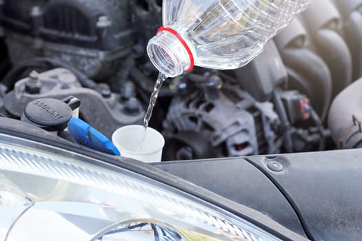 Pouring distilled water (ecological alternative to washing fluid) to washer tank in car, detail on stream of clear liquid flowing