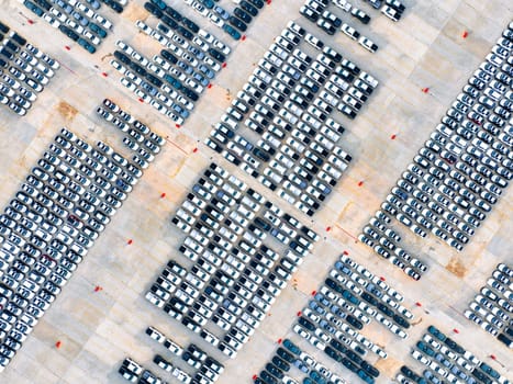 Aerial view of automotive logistics. Factory parking lot filled with rows of new cars. Modern vehicle production and distribution. Import or export operations at expansive port terminal facilities