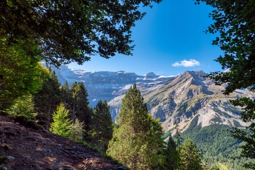 The Cirque of Gavarnie, french Pyrenes mountains. The mountains are covered in snow and the sky is cloudy. The river is surrounded by a lush green valley