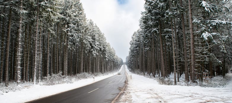 Road through a snow covered forest, slippery and frosty street in winter, empty highway in cold temperature, seasonal weather and landscape