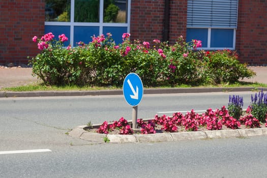 Traffic island on road with arrow signpost and flower bed, Germany