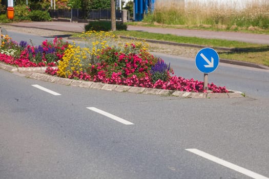 Traffic island on road with arrow signpost and flower bed, Germany