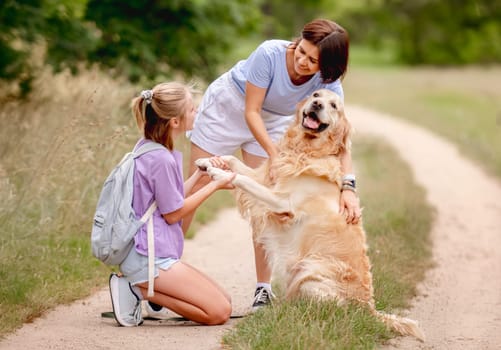 Daughter And Mother Teaching Golden Retriever Dog To Give Its Paw Happily During The Summer