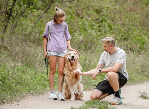 Daughter And Father Happily Teaching Golden Retriever Dog To Give A Paw During A Summer Day