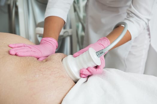 Closeup photo of fat man with big belly having cavitation procedure removing cellulite on abdomen in modern beauty clinic