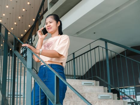 An attractive, Asian woman in fashionable is talking on the phone while standing in front of the building or shopping mall. People and wireless technology concepts, City life, Wireless technology.