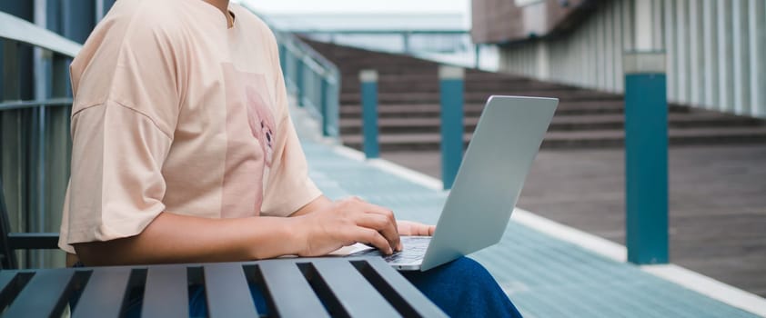 Confident female entrepreneur sits on a metal table next to the corridor in a modern city, She working with laptop computer and online marketing service, Working on laptop connected to public wi-fi.