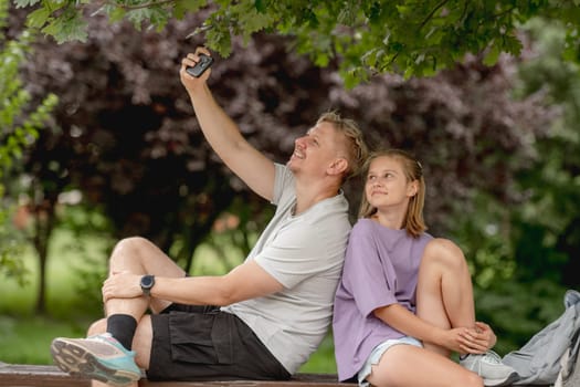 Father And Daughter Taking A Selfie On A Summer Bench, Enjoying Family Time Together