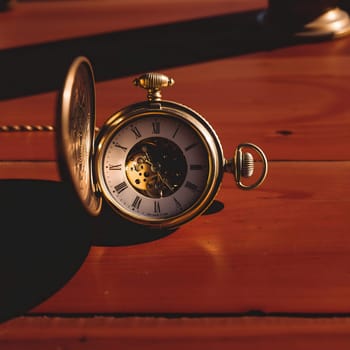 An antique pocket watch is opened and positioned on a warm wooden table, showcasing its intricate gears, illuminated by the soft glow of golden hour sunlight.