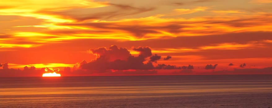 As the sun dips below the horizon, vibrant orange and red hues fill the sky, reflecting beautifully on the tranquil ocean surface, creating a serene and picturesque evening.