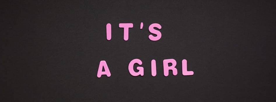 Creative pink text made from plastic letters It's a girl writing on black paper background with copy space. Baby shower concept, celebration card template