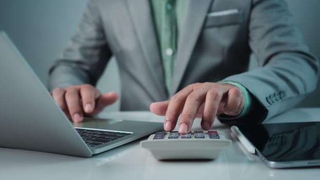 Accountant working with calculator and paperwork, Businessman calculating taxes and finances on laptop at corporate desk, Financial success, Economy concept, Man managing budget and market statistics.