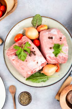 Slices of raw pork meat and vegetables on rustic wooden background.