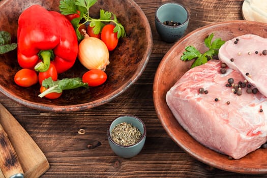 Slices of raw pork meat and vegetables on rustic wooden background.