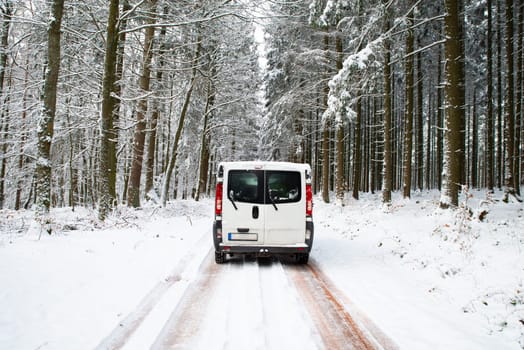 Camper Van driving on a road through a snow covered forest in winter, adventure vacation and lifestyle in the woodlands, slippery highway