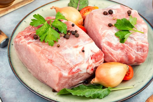 Plate with two pieces of raw meat and fresh vegetables for cooking.