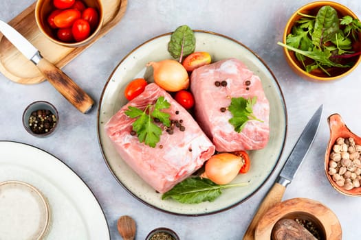 Plate with two pieces of raw meat and fresh vegetables for cooking.
