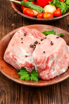 Plate with two pieces of raw meat and fresh vegetables for cooking.