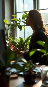 A person practices meditation in a serene workspace filled with lush indoor plants, enjoying the tranquility of natural light filtering through large windows.