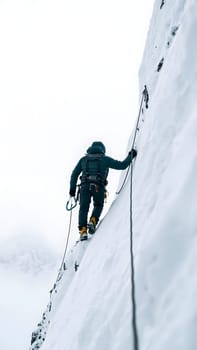 A climber expertly navigates a steep, snow-covered slope, using safety gear and harnesses. The backdrop features a remote, rugged mountain landscape under cloudy skies.