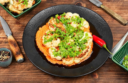 Roasted cauliflower florets are drizzled with creamy tahini sauce and sprinkled with pomegranate served on a rustic wooden table.