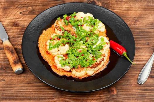 Roasted cauliflower florets are drizzled with creamy tahini sauce and sprinkled with pomegranate served on a rustic wooden table.