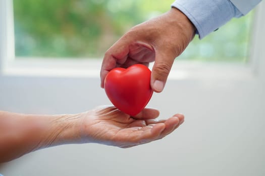 Asian elder senior woman patient holding red heart in hospital.
