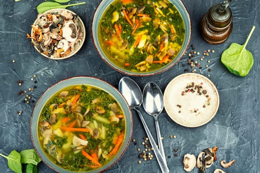 A bowl of soup with mushrooms and spinach leaves.