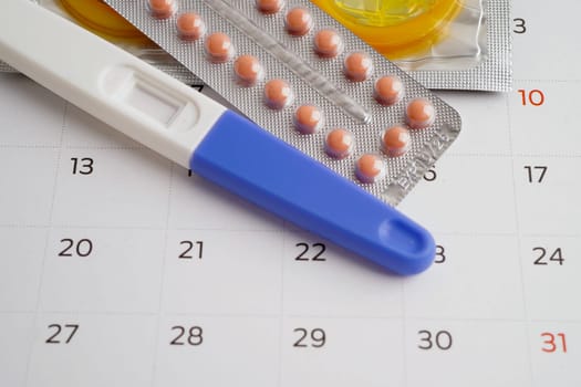 Pregnancy test with birth control pills and condom for female on calendar, ovulation day.