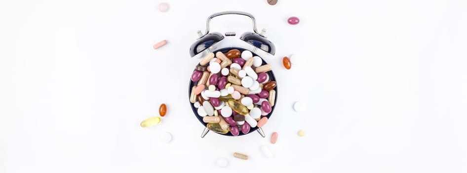 Nutritional supplement color pills on black alarm clock face isolated on white background with copy space. Template for feminine beauty blog social media. Female healthcare concept