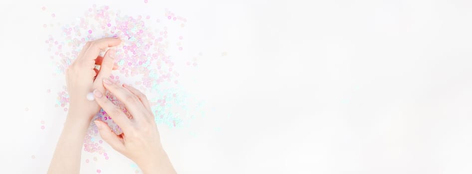 Woman moisturizing her hands with cosmetic cream lotion white pearl pastel confetti sparkles background with copy space. Creative conceptual top view flat lay backdrop for your beauty blog text design