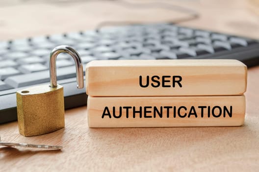 User Authentication text engraved on wooden blocks with padlock and PC keyboard background.