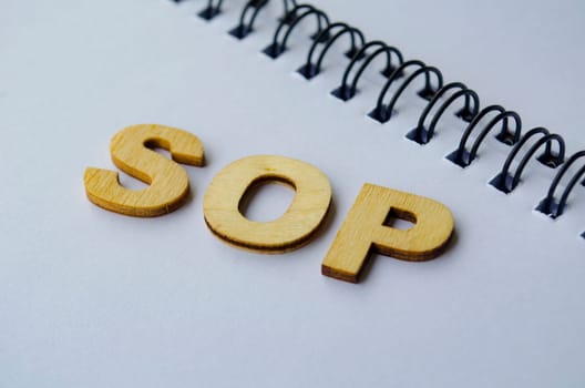 Top view of SOP wooden letters on white notepad. Standard Operating Procedure concept.