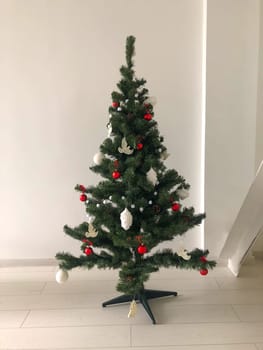 A minimalist Christmas tree decorating a modern living space, adorned with red, white, and silver ornaments. Simplicity design and festive charm to the clean, contemporary room. Minimalistic xmas decor concept.