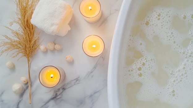 Luxurious bath scene with lit candles, white towel, and pampas grass on marble surface, featuring bubbles and soothing ambiance for relaxation.