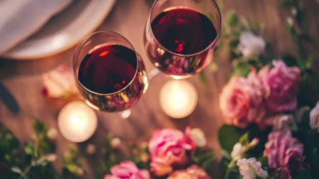 Intimate setting with two glasses of red wine, lit candles, and pink roses, creating a romantic atmosphere for a special occasion or date night.