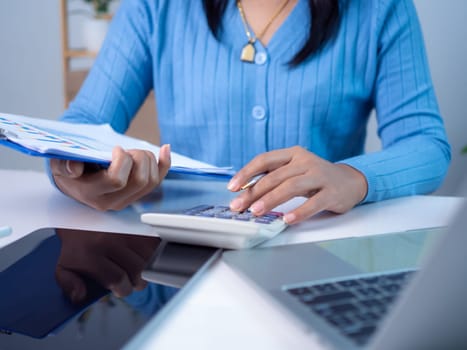 Businesswoman hand working with finances about cost and calculator and laptop with tablet on desk at office in morning light, Business accounting concept, Calculating or checking balance.